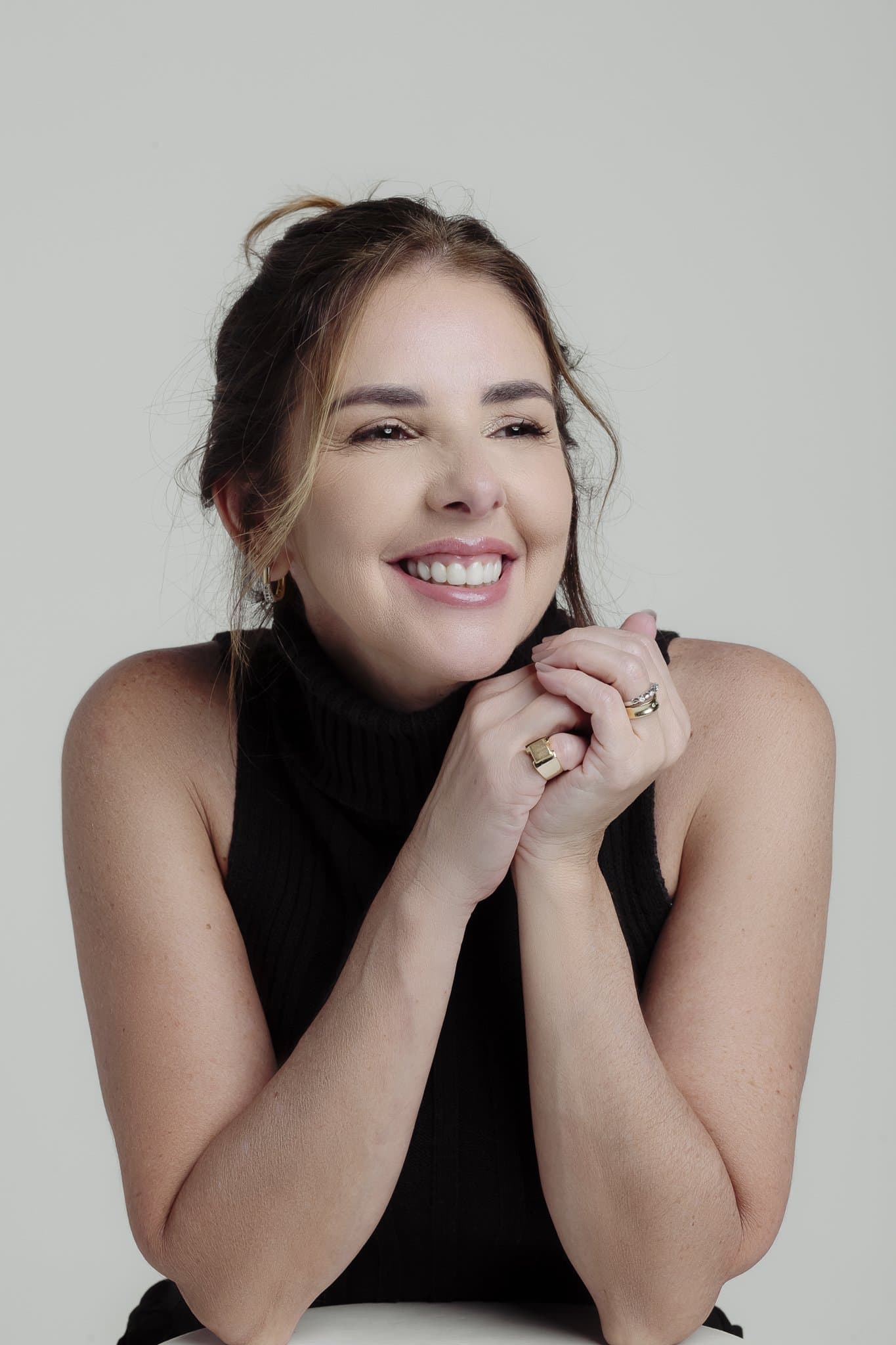 Anna Braga sorrindo, com as mãos junto ao rosto