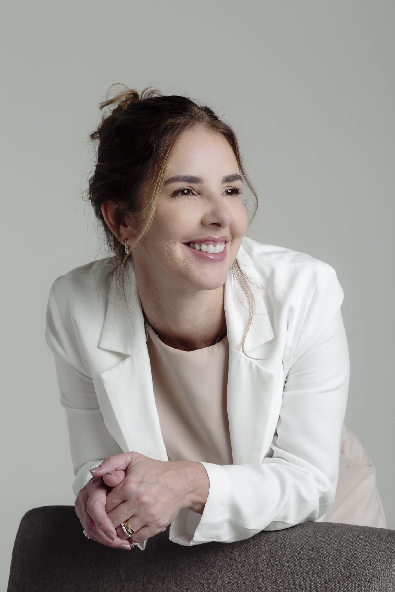 Anna Braga sorrindo, apoiada no encosto de uma poltrona.